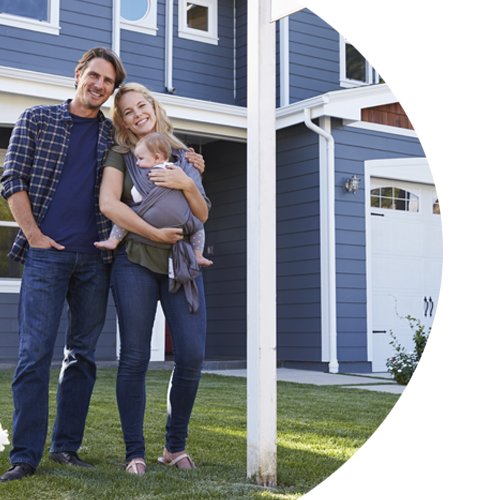 Young, smiling couple holding their infant child while standing in front of their home